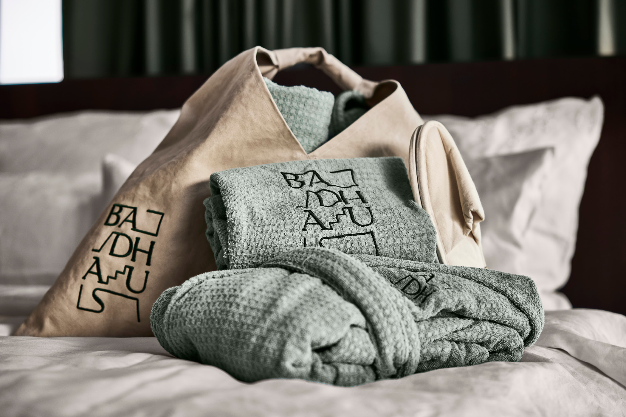 Set aus grünen Badetextilien mit Badhaus-Logo auf Bett