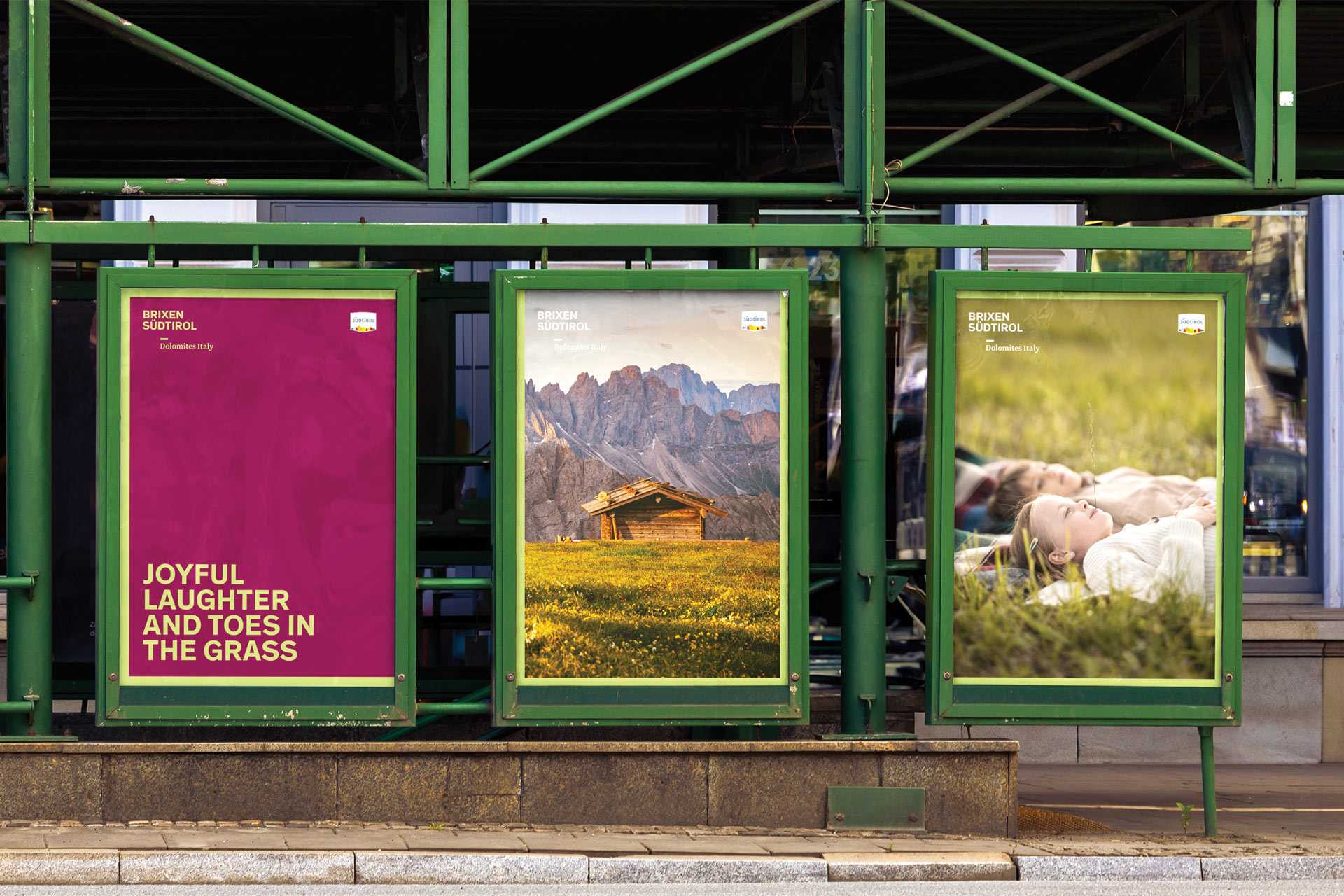 Drei Plakate in grünem Rahmen in Brixen, Südtirol, mit Text und Landschaft.