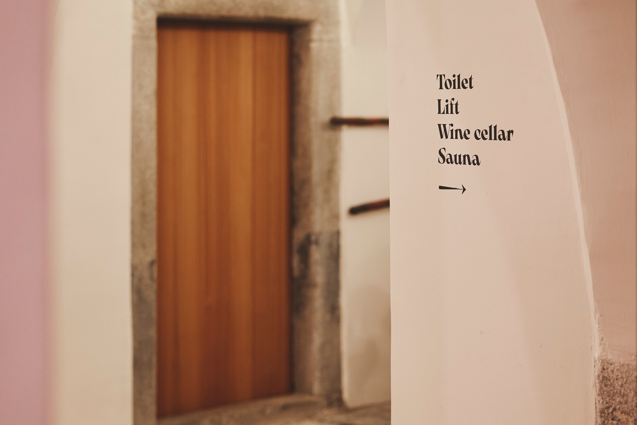 Holztür und Wandbeschriftung mit Hinweisen zu Toilette, Lift, Weinkeller, Sauna