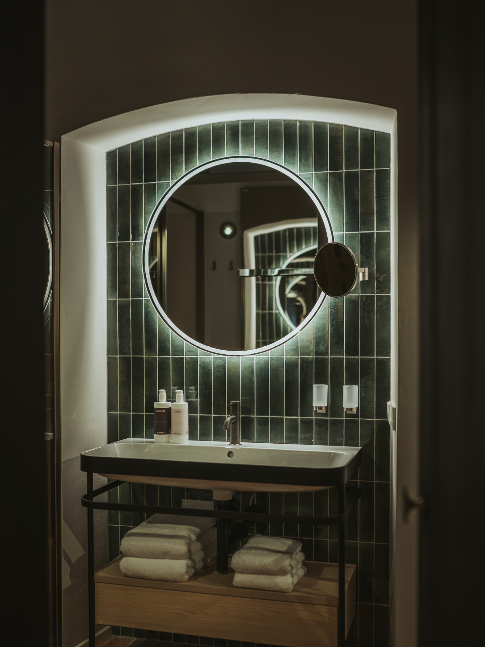 Modernes Badezimmer mit großem, rundem Spiegel und grünen Fliesen