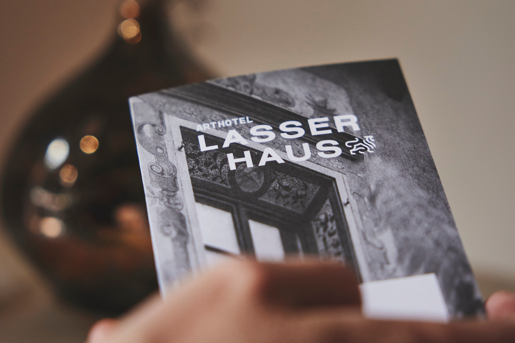 Hand hält Broschüre mit ArtHotel Lasserhaus Titel