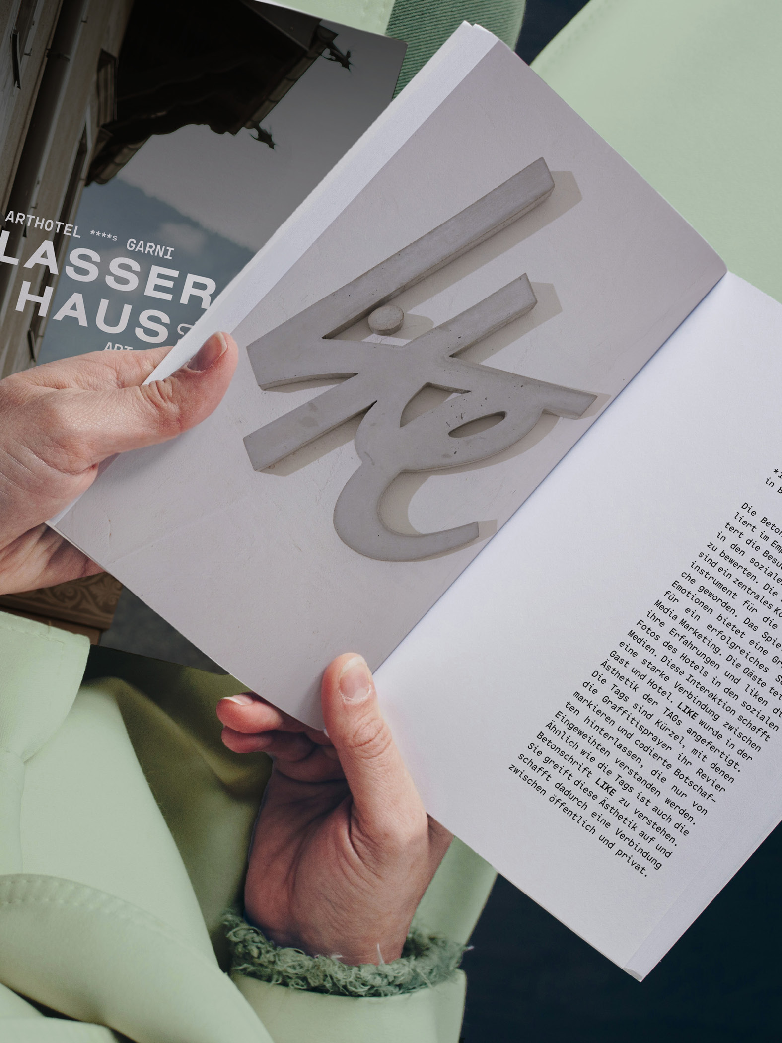 Person blättert Buch mit Skulpturfoto und Texten, Lasserhaus Broschüre darunter.