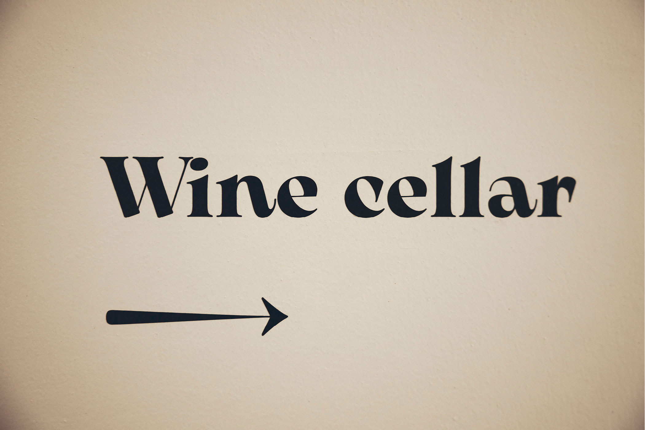 Schriftzug 'Wine cellar' mit Pfeil auf beiger Wand