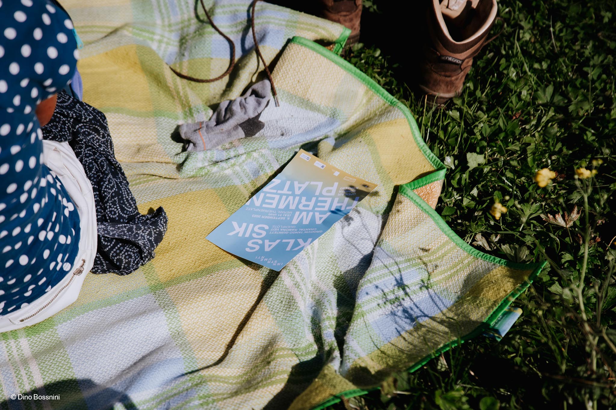 Broschüre auf Picknickdecke neben Schuhen im Gras