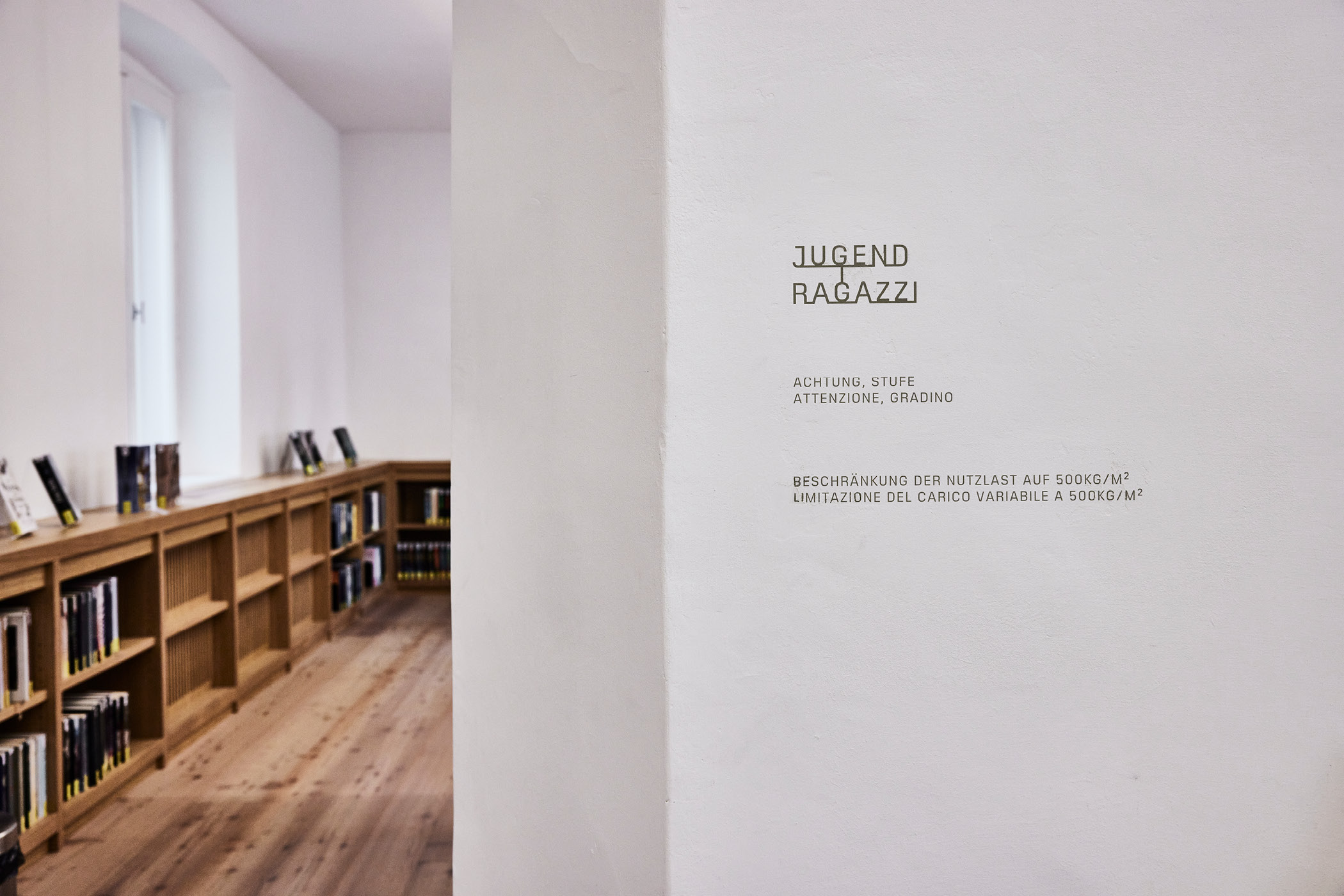 Bücherregale in Brixner Stadtbibliothek, Warnschild an weißer Wand